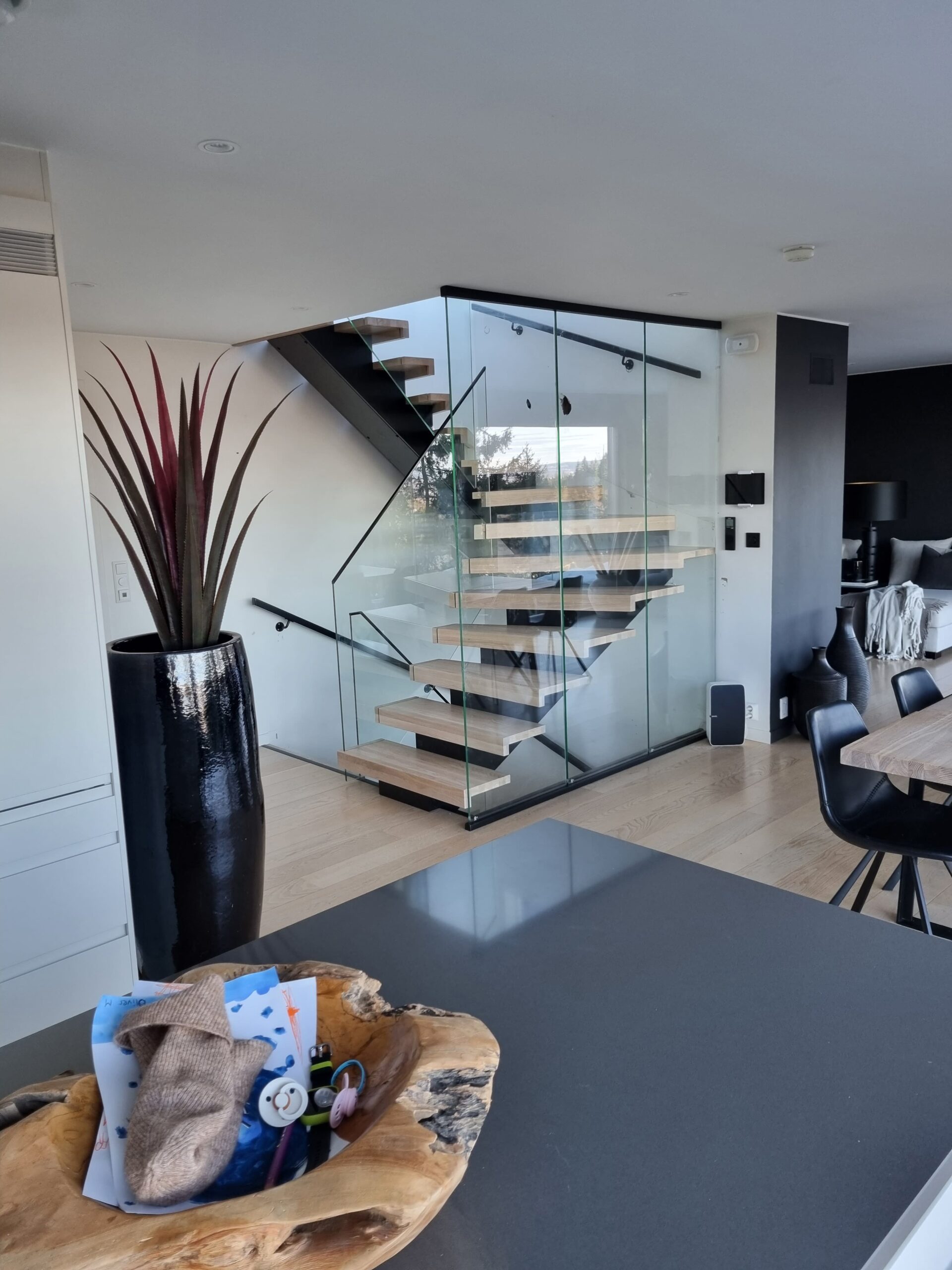 Treppe mit Glasgeländer aus hellem Holz mit schwarzem Mittelholm